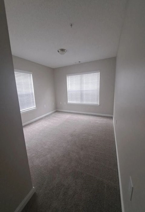 an empty room with a carpeted floor and two windows